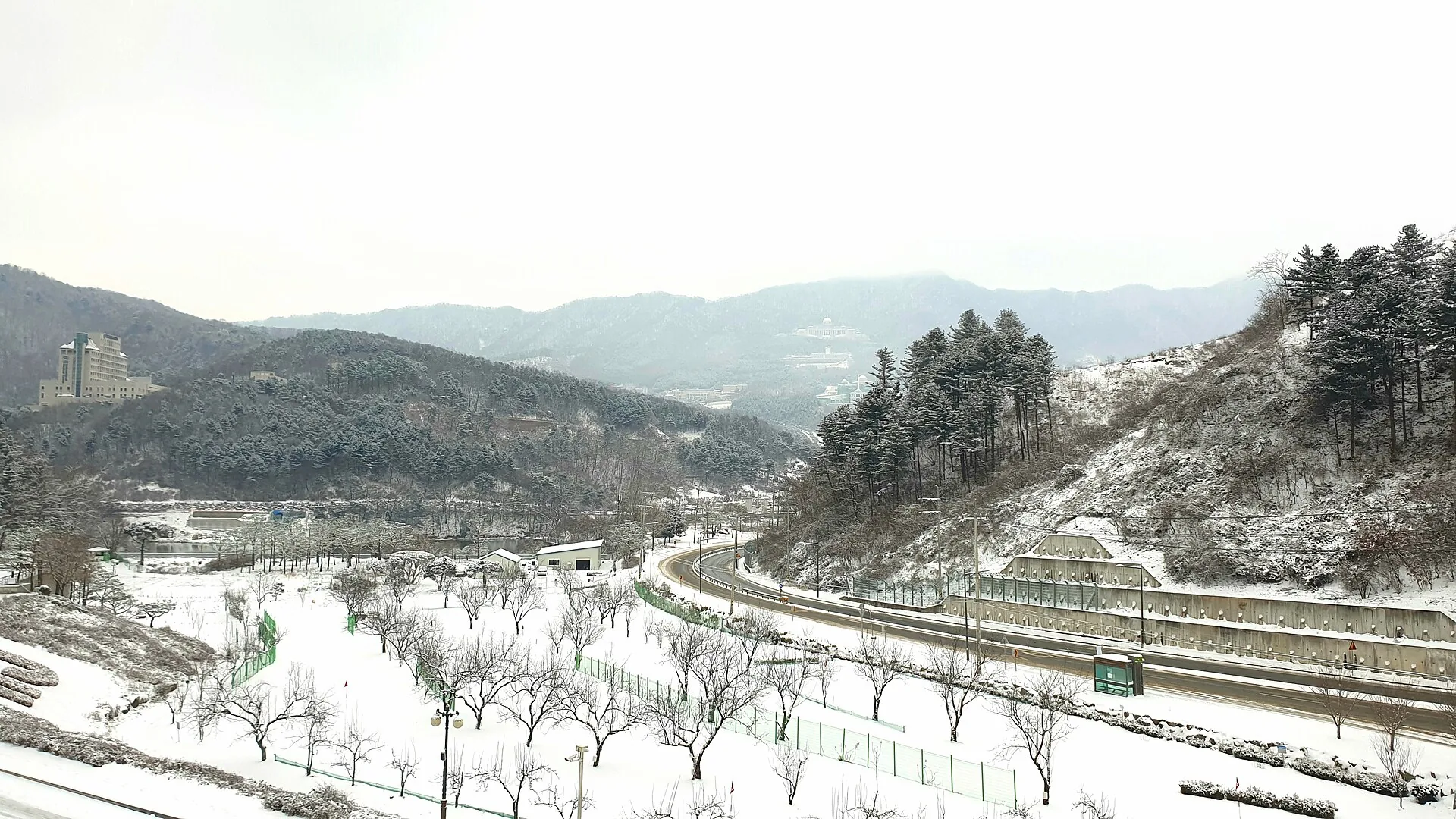 Vale montanhoso coreano coberto de neve, com estrada e edifícios
