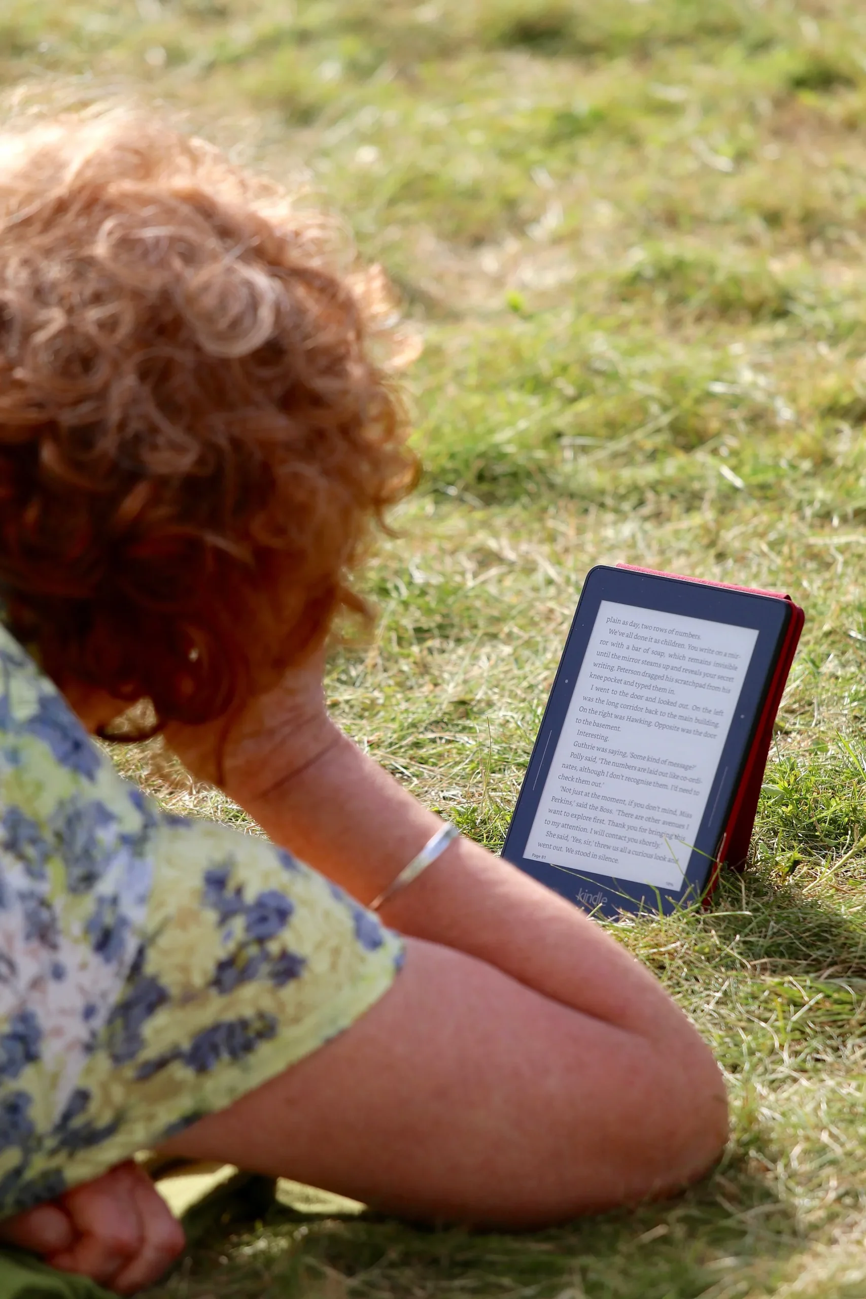 Pessoa lê num Kindle sentada na relva ao ar livre